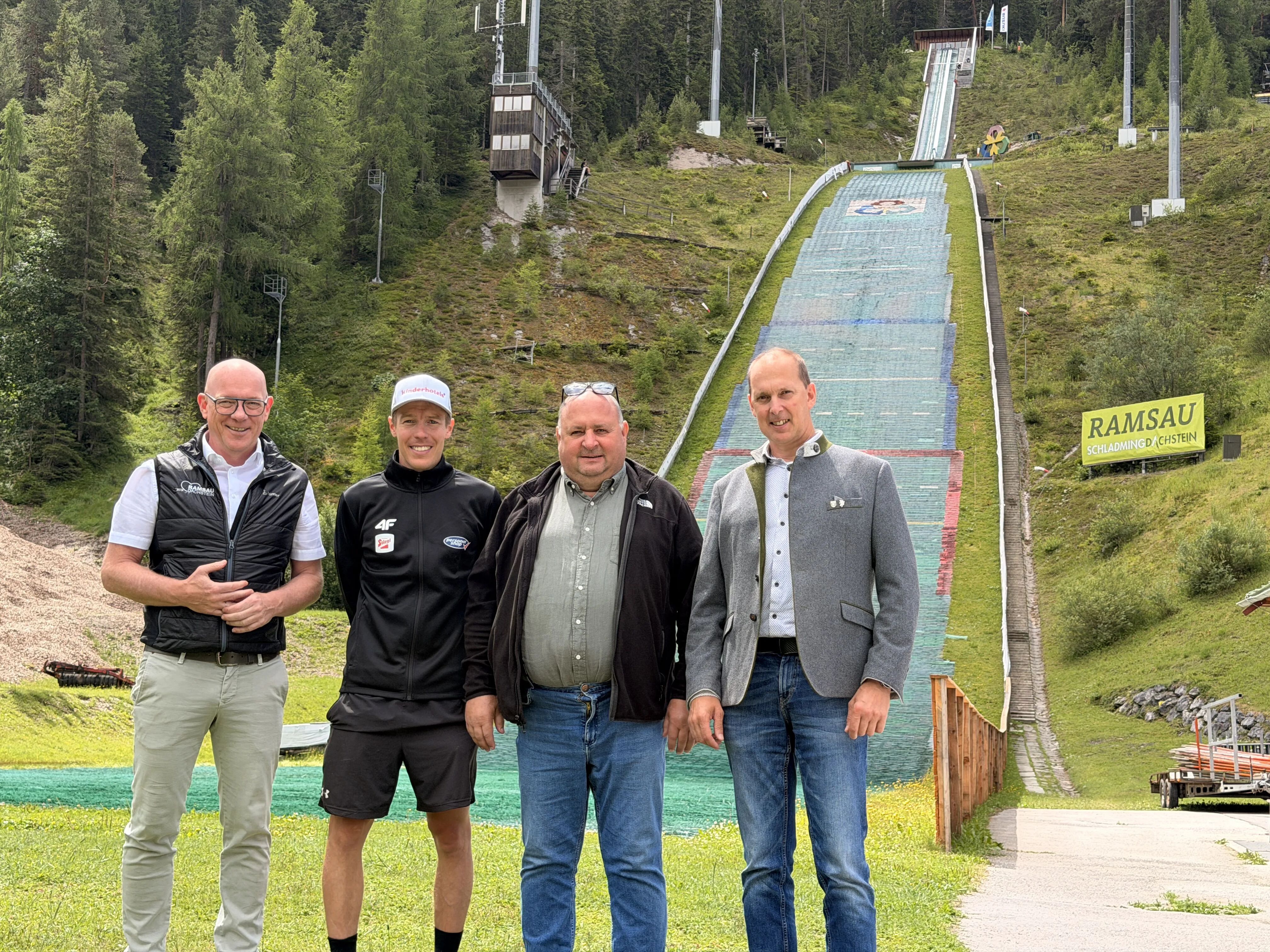 Vier Männer vor einer Skisprungschanze